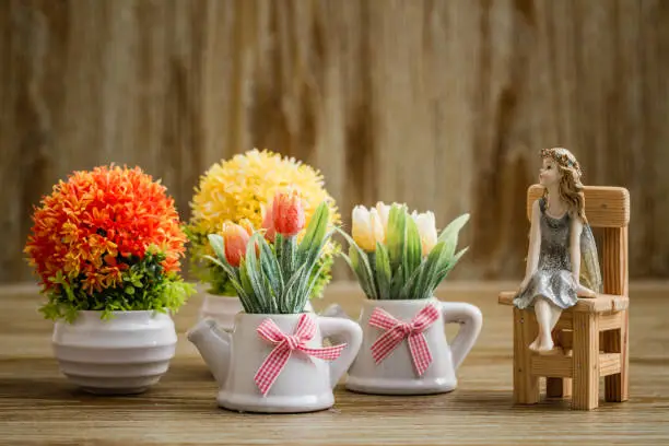 Decorative artificial flowers and angel trinket on wooden background