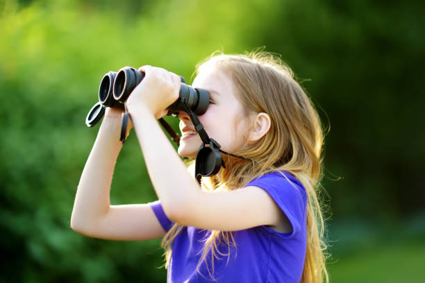 istock Funny little girl looking through binoculars on sunny summer day 975866746