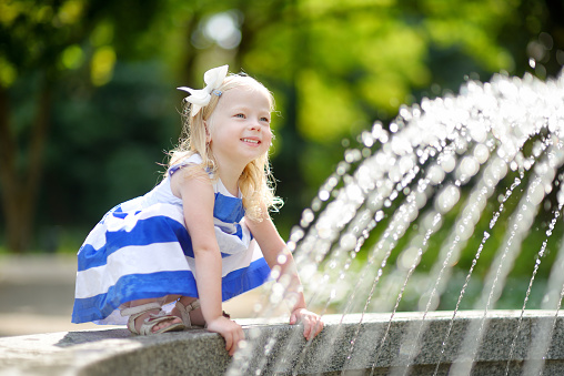 Cute little girl playing with a city fountain on hot and sunny summer day