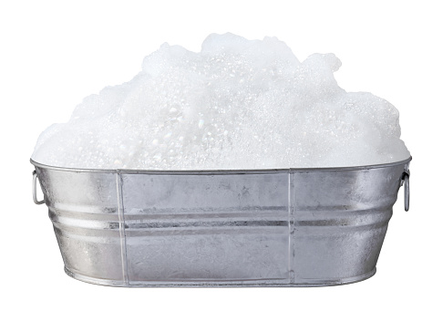 Soap Suds and Bubbles in a antique galvanized tub.  The tub is gray and shiny and shows reflections.  This container was used as a bathtub on farms before indoor plumbing.