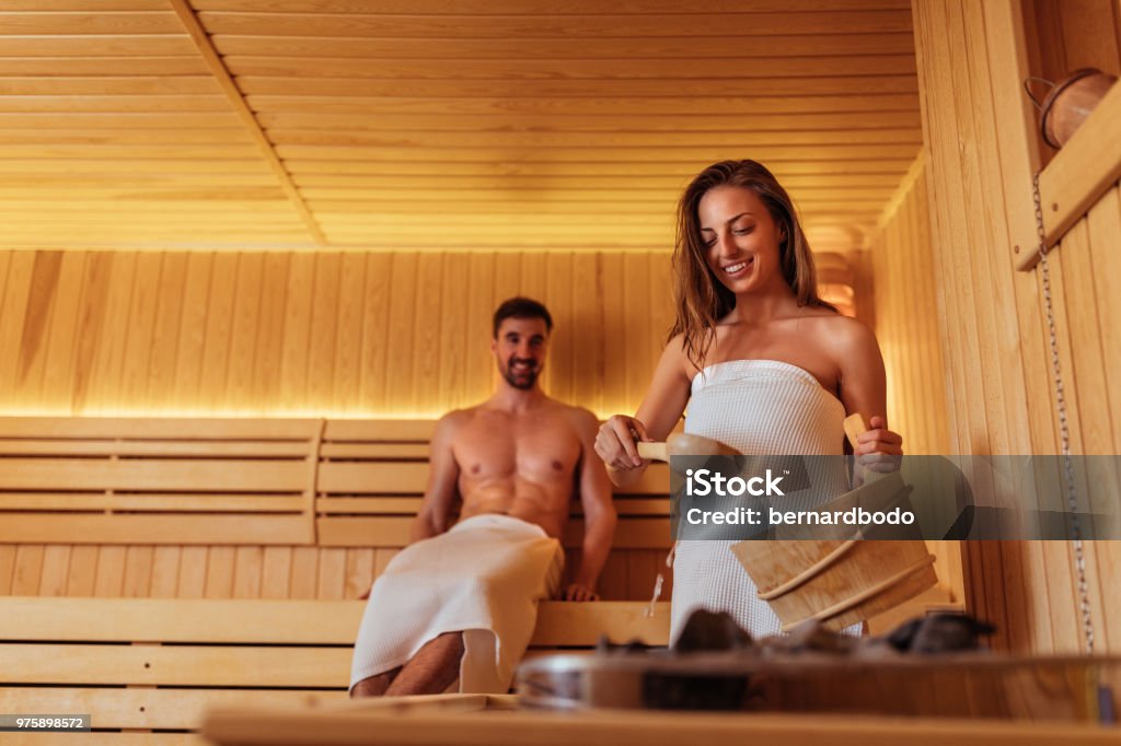 She's steaming it up Shot of a young woman pouring water over sauna rocks Sauna Stock Photo