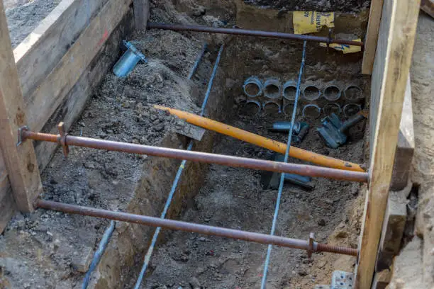 View into a construction pit with exposed pipes of a power line