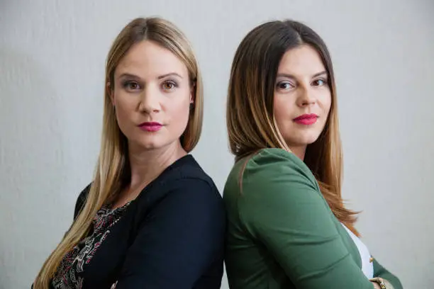 Portrait of two confident businesswomen standing back to back.