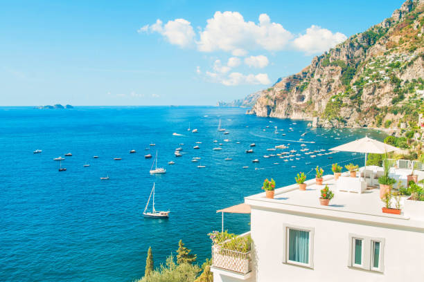 white holiday villa with balcony and rooftop terrace facing Mediterranean sea with mountains at background on sunny summer day, Positano, Amalfi coast, Italy