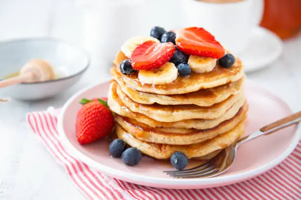 Stack of homemade pancakes with strawberries, banana and blackberries on a pink plate