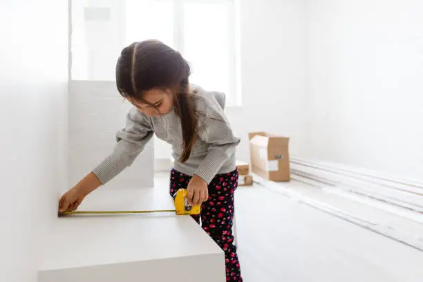 Little smiling girl holding tape-measure apartment repair wall repair renovation house renovation home