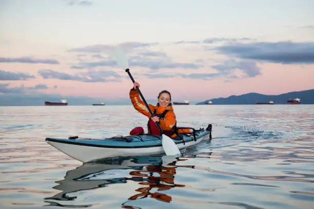 Adventurous woman is sea kayaking near Downtown Vancouver, British Columbia, Canada, during a vibrant sunrise. Concept of Adventure and Fitness