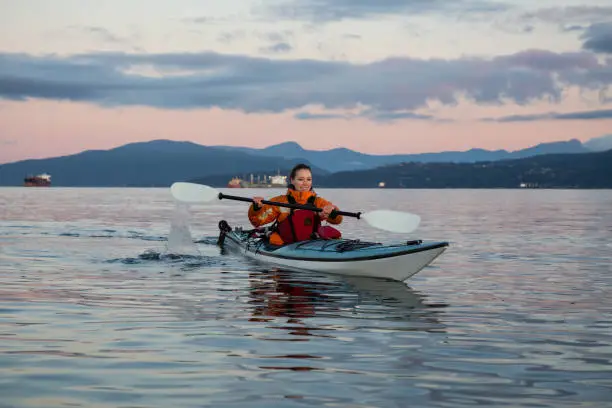 Adventurous woman is sea kayaking near Downtown Vancouver, British Columbia, Canada, during a vibrant sunrise. Concept of Adventure and Fitness