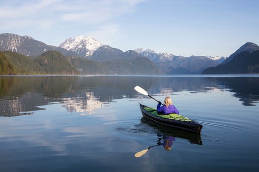 Adventurous girl is kayaking on an inflatable kayak on a beautiful lake with mountains in the background. Taken in Stave Lake, East of Vancouver, British Columbia, Canada.
