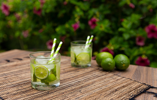 Brazilian drink Caipirinha with ingredients on wooden table and plants on the background