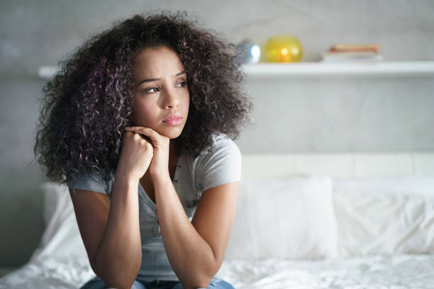 Depressed Hispanic Girl With Sad Emotions And Feelings Lonely young latina woman sitting on bed. Depressed hispanic girl at home, looking away with sad expression. anxiety stock pictures, royalty-free photos & images