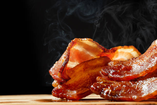 Hot Bacon With Steam Isolated on Black Closeup of slices of crispy hot freshly cooked bacon with copy space in black background cooked bacon slice stock pictures, royalty-free photos & images