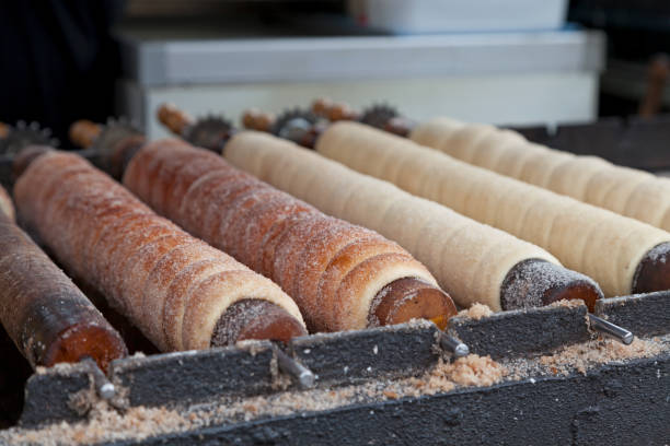 Row of Trdelník on their sticks Trdelník is a kind of spit cake. It is made from rolled dough that is wrapped around a stick, then grilled and topped with sugar and walnut mix. trdelník stock pictures, royalty-free photos & images