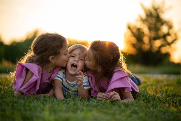 Twin sisters kissing little boy lying on grass