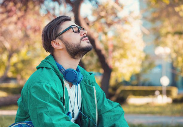 Man enjoying time in park Hipster man in headphones and glasses keeping eyes closed and enjoying fresh air in summer park breath vapor stock pictures, royalty-free photos & images