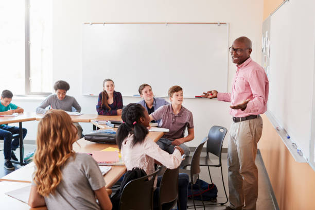 istock Male High School Tutor Standing At Whiteboard Teaching Class 976319066