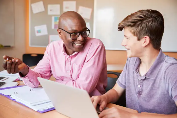 Photo of High School Tutor Giving Male Student One To One Tuition At Desk