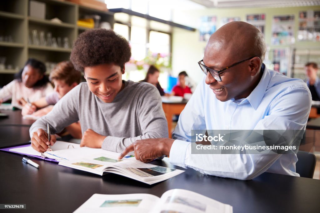 Tutor del liceo seduto alla scrivania con studente maschio in classe di biologia - Foto stock royalty-free di Insegnante