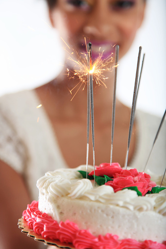 Young woman with cake. Focus is on cake and lit sparklers with teenager blurred in background.