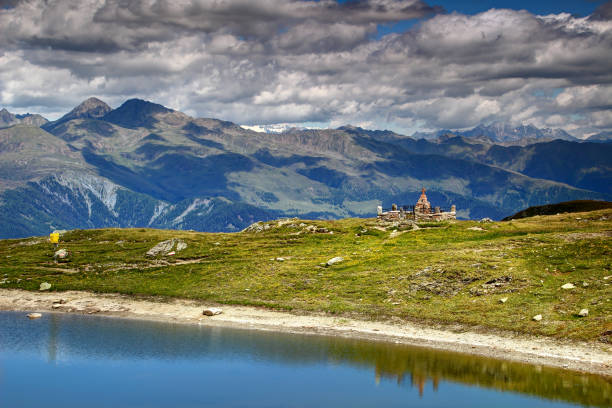 Austrian soldiers' First World War grave in sunlit Karnische Alpen meadow on Hochgranten lakes shore, Karnischer Hohenweg Traversata Carnica Friedensweg Via della Pace, Italian border Osttirol Austria
