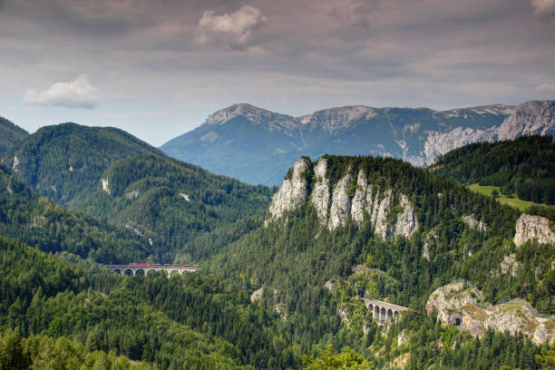 Freight train on Semmering railway crosses Kalte Rinne viaduct under Polleroswand among green forests of Semmering Pass with Rax Schneeberg Group in background, Northern Limestone Alps Austria Europe