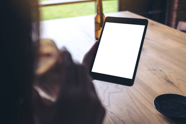 istock Mockup image of a woman holding black tablet pc with blank white desktop screen while drinking coffee in cafe 976460174
