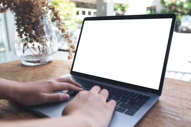 istock Mockup image of hands using and touching laptop with blank white desktop screen on wooden table in cafe 976460222