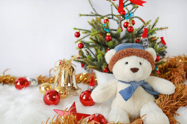 a toy teddy bear in pine cone with a cap placed next to a decorative fir tree on a background of brown green wood