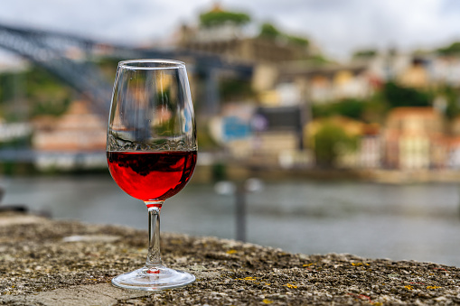 Glass of port wine on an old stone wall at an outdoor restaurant with the Douro river  and Dom Luis I bridge blurred in the background in Porto, Portugal