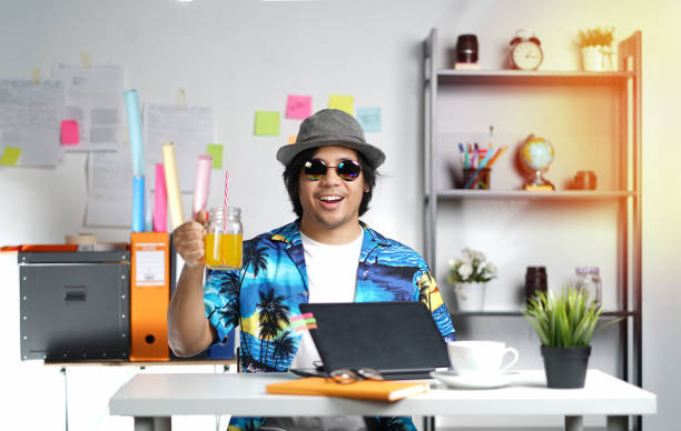 stylish young man holding orange juice while working on summer vacation season at office - roupa morna imagens e fotografias de stock