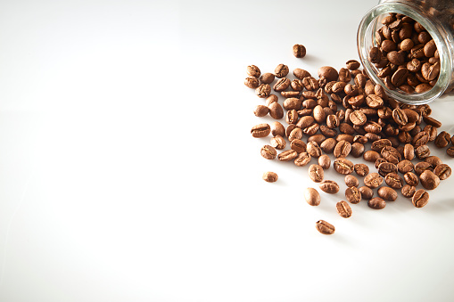 multiple roasted coffee beans poured from clear glass on white background, flat lay