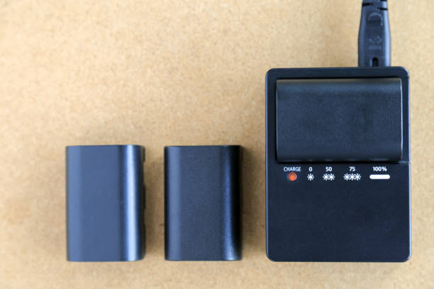 istock Camera battery is charging on battery charger on wooden table. 976522214