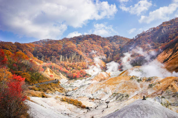 Beautiful sunny day at Noboribetsu Jigokudani or Hell Valley in Hokkaido, Japan. Autumn season, red leaves, blue sky and sulfur gas steaming out from ground. stock photo