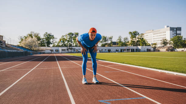 istock Athletic handsome male relaxing after intense workout and running on stadium. Athlete taking rest with hands resting on knees after a jogging and run standing on race track outdoor. People and sport 976572806