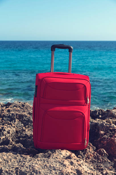 istock Rocky sea shore and red suitcase. Selective focus 976579042