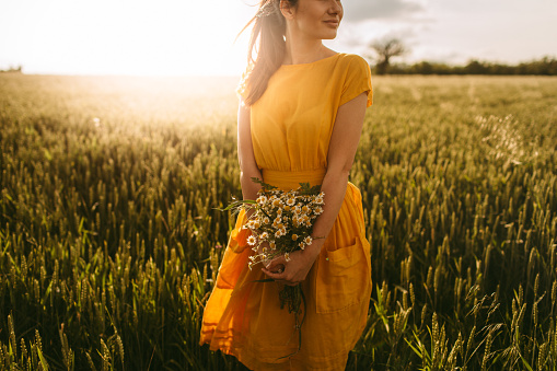 Young girl holding chamomile plant in her hands and enjoying the calm meadow