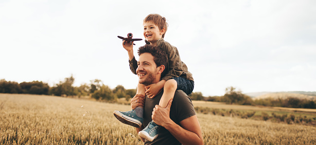 Young boy playing with an airplane while sitting on his father's shoulders