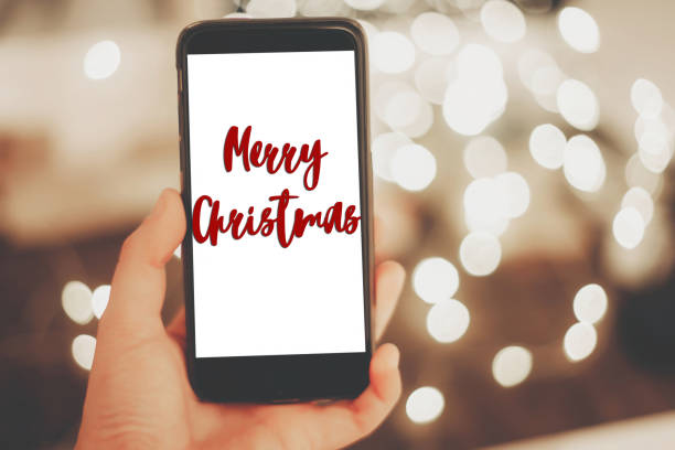 istock merry christmas text sign on hand holding smart phone with empty screen on background of christmas lights in evening. space for text. happy holidays. vintage tone. greetings 976591818