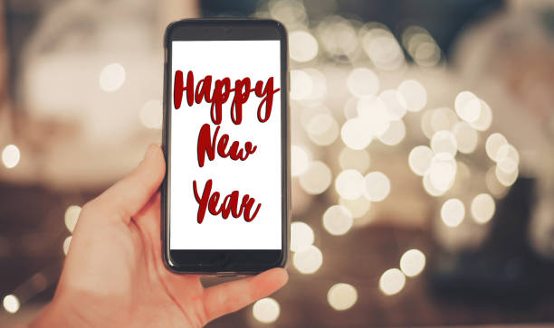 istock happy new year text sign on hand holding smart phone with empty screen on background of christmas lights in evening. space for text. happy holidays. vintage tone. christmas greetings 976591840