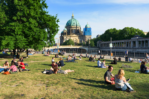 Berlin, Germany - May 25, 2018: People relaxing at the James-Simon Park in Berlin, Germany, with the Spree River and the Berliner Dom, the Cathedral of Berlin, in the background