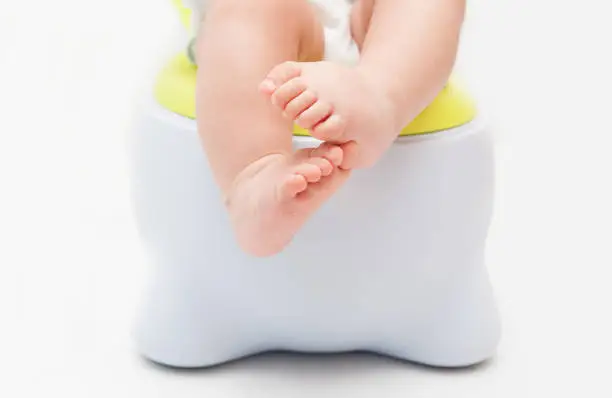 Children's legs hanging down from a chamber-pot.