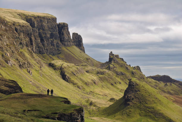 квиринг, остров скай, шотландия - bizarre скалистый пейзаж с двумя человеческими фигурами, стоящими на скале на переднем плане - trotternish стоковые фото и изображения