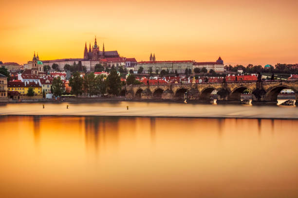Castle of Prague and Charles bridge reflected on Vltava river at sunset Long exposure of Castle of Prague and Charles bridge reflected in the Vltava River in Prague. Czech Republic clear sky night sunset riverbank stock pictures, royalty-free photos & images