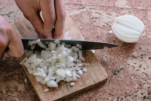 Man gently cuts the onion into small pieces and takes a wooden board with onion from the table