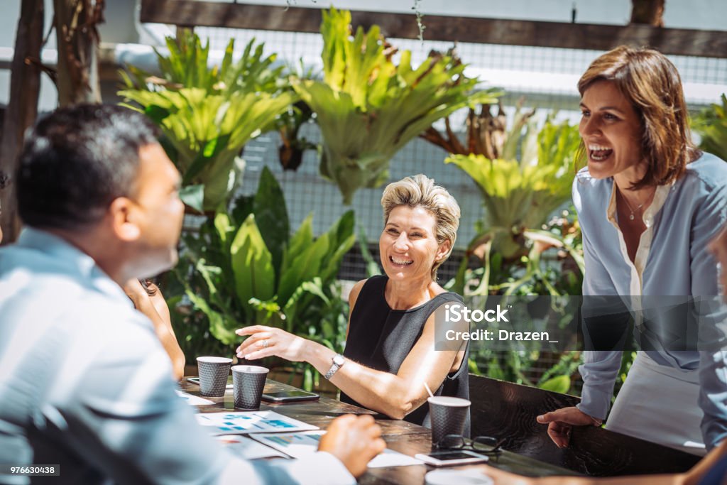 Teamwork with colleagues in outdoor cafe Group of professionals having a business meeting in outdoor cafe or restaurant where they discuss the investment ideas and cooperation plans while drinking coffee. Group of businesswomen and businessmen enjoying working together Responsible Business Stock Photo