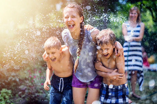 Hot summer day. Mother splashing laughing kids in back yard.\nNikon D850