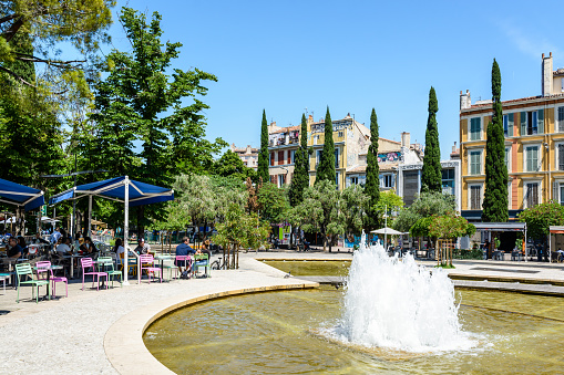 Marseille, France - May 23, 2018: The fountain of the cours Julien, a large pedestrian, very popular and trendy square, with basins, cypress and olive trees, shops, bars and restaurants with terrace.