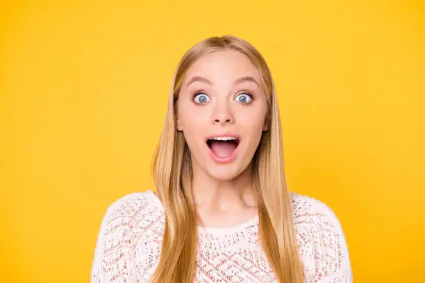Photo of Head shot portrait of astonished surprised girl with wide open mouth eyes looking at camera isolated on vivid bright yellow background