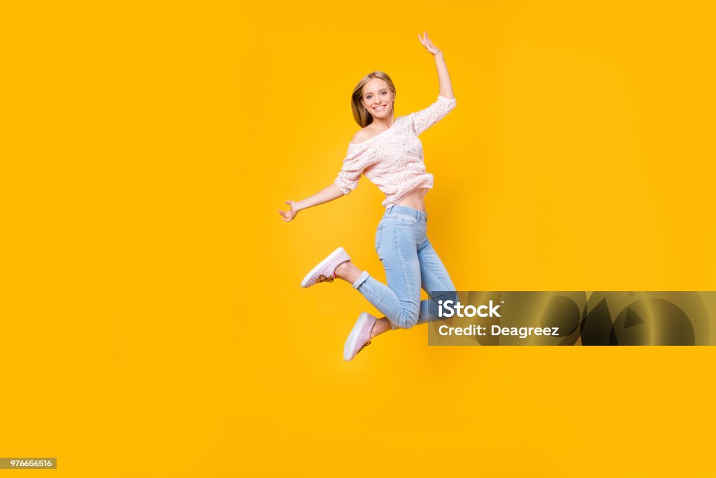 Portrait of playful crazy girl jumping in the air looking at camera enjoying weekend having perfect mood isolated on yellow background Women Stock Photo