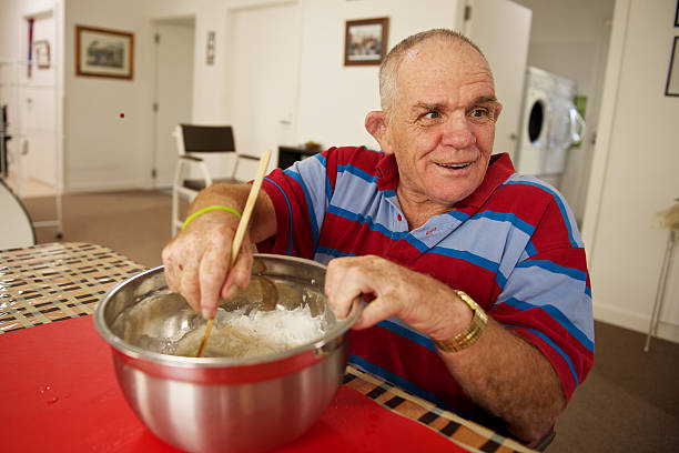 Senior man with a disability at home mixing flour. Senior man with a disability at home mixing flour.  He was cooking muffins for supper in his kitchen. disabled adult stock pictures, royalty-free photos & images